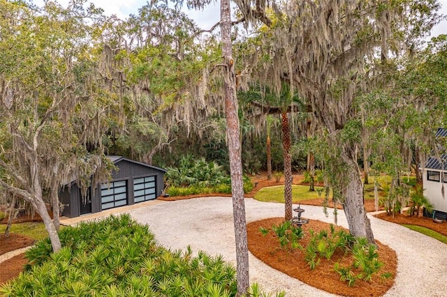 view of community featuring a detached garage, curved driveway, and an outdoor structure