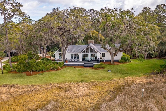 back of house with metal roof, a chimney, a deck, and a yard