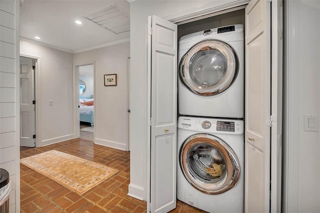 clothes washing area featuring stacked washer and dryer, laundry area, baseboards, brick floor, and crown molding