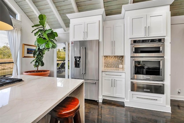 kitchen featuring dark wood finished floors, decorative backsplash, appliances with stainless steel finishes, light stone countertops, and a warming drawer