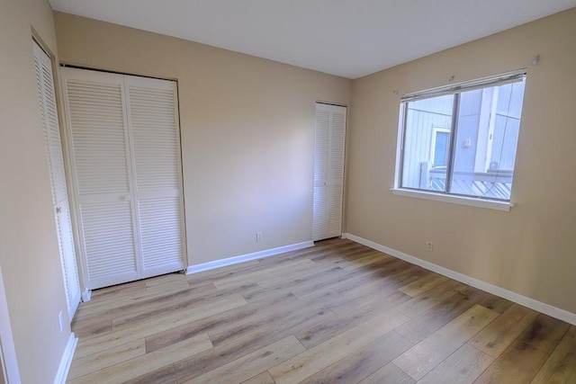 unfurnished bedroom with two closets, light wood finished floors, and baseboards