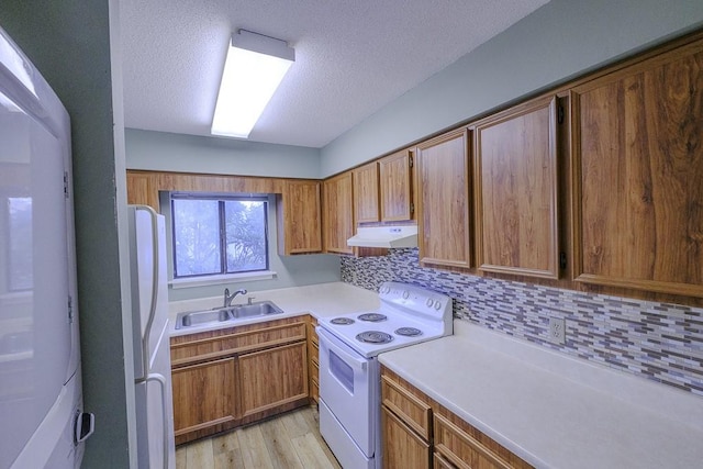 kitchen with a sink, decorative backsplash, under cabinet range hood, white appliances, and light countertops
