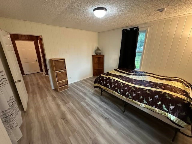 bedroom featuring wood walls, wood-type flooring, and a textured ceiling