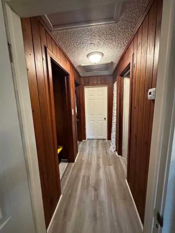 corridor with wooden walls, light hardwood / wood-style flooring, crown molding, and a textured ceiling