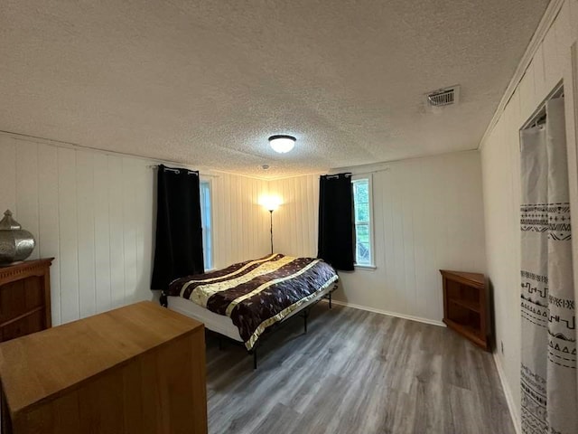 bedroom featuring a textured ceiling, hardwood / wood-style flooring, and wood walls