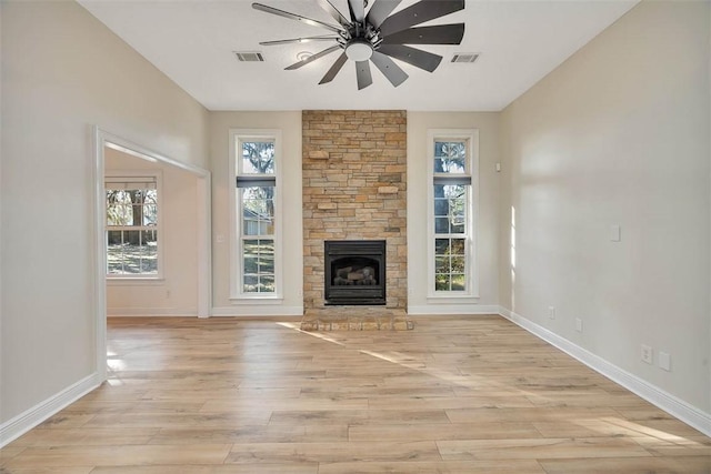 unfurnished living room featuring a ceiling fan, visible vents, a fireplace, and light wood finished floors