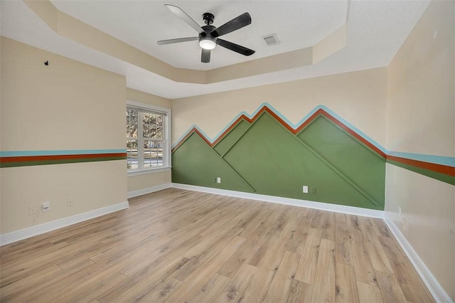 spare room featuring ceiling fan, a tray ceiling, light wood-style flooring, and baseboards