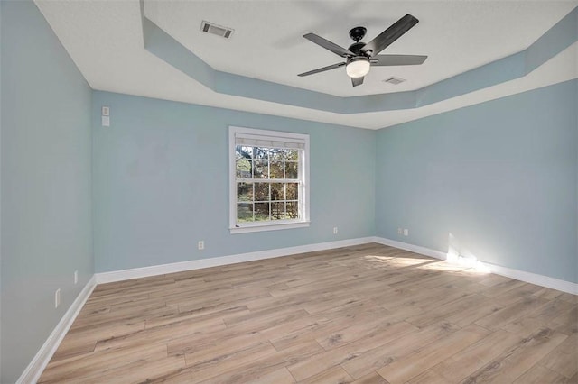 spare room featuring light wood-style flooring, visible vents, a raised ceiling, and baseboards