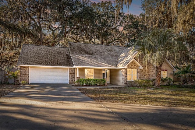 view of front of property with driveway, roof with shingles, an attached garage, a front lawn, and brick siding