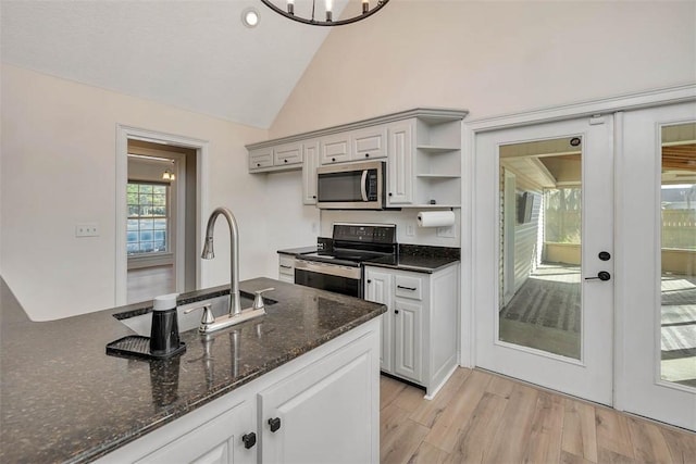 kitchen featuring light wood finished floors, dark stone counters, appliances with stainless steel finishes, open shelves, and a sink