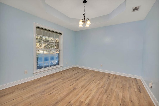 empty room with visible vents, baseboards, an inviting chandelier, a tray ceiling, and light wood-type flooring