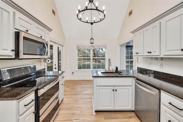 kitchen featuring a peninsula, hanging light fixtures, stainless steel appliances, light wood-style floors, and a sink