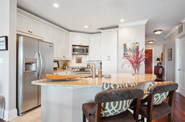 kitchen featuring a kitchen breakfast bar, ornamental molding, stainless steel appliances, white cabinets, and light hardwood / wood-style floors