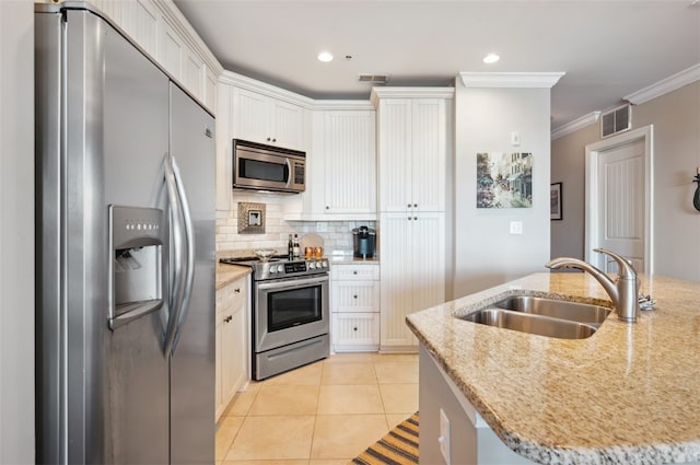 kitchen with light stone counters, stainless steel appliances, a kitchen island with sink, crown molding, and white cabinets