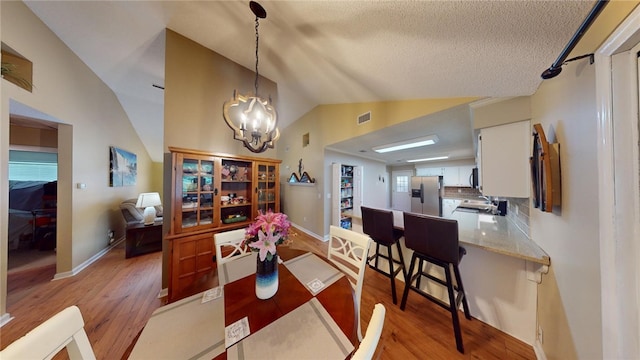 dining space featuring an inviting chandelier, sink, vaulted ceiling, a textured ceiling, and light hardwood / wood-style floors