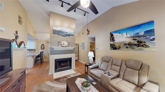 living room featuring track lighting, ceiling fan, high vaulted ceiling, light hardwood / wood-style flooring, and a tiled fireplace