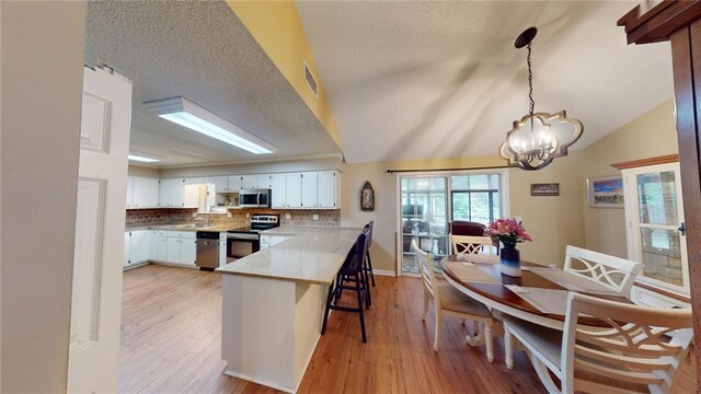 kitchen featuring kitchen peninsula, vaulted ceiling, a textured ceiling, white cabinets, and appliances with stainless steel finishes