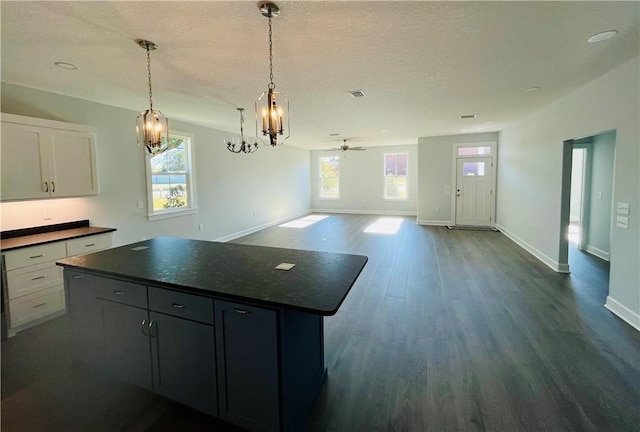 kitchen with white cabinetry, decorative light fixtures, dark wood-type flooring, a kitchen island, and ceiling fan with notable chandelier