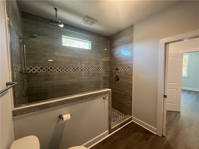 bathroom with hardwood / wood-style floors, tiled shower, and toilet