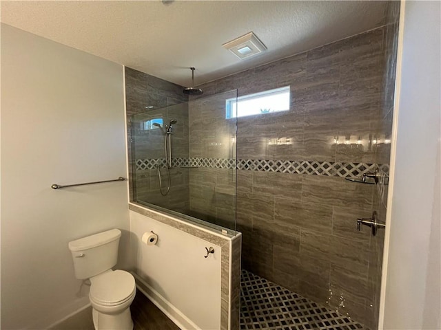 bathroom with toilet, a textured ceiling, and a tile shower