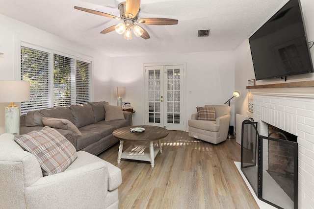 living room featuring french doors, a textured ceiling, ceiling fan, light hardwood / wood-style flooring, and a fireplace