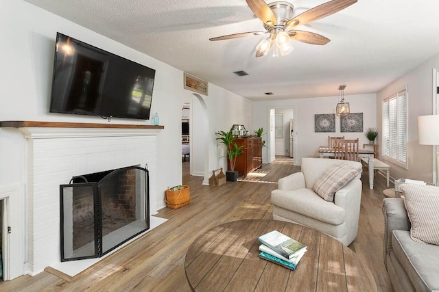 living room with hardwood / wood-style floors, ceiling fan, a fireplace, and a textured ceiling