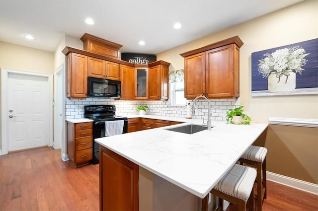 kitchen with a breakfast bar area, a peninsula, wood finished floors, a sink, and black appliances