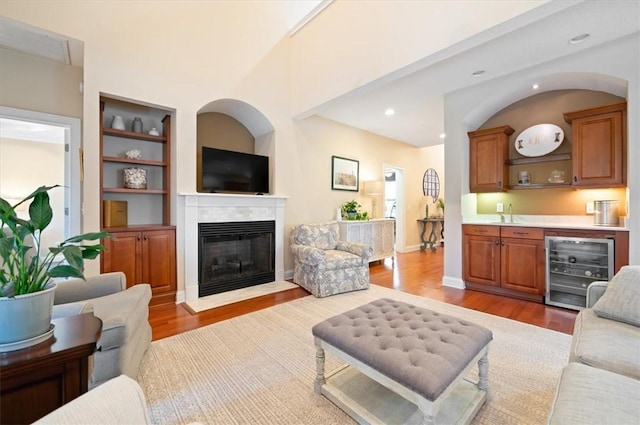 living area with a fireplace with flush hearth, wine cooler, wood finished floors, built in shelves, and recessed lighting