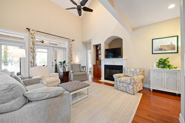 living area featuring a fireplace with flush hearth, ceiling fan, wood finished floors, high vaulted ceiling, and baseboards