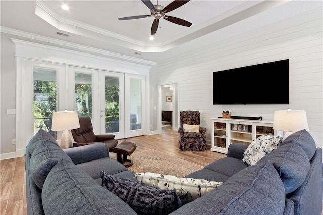 living room featuring ceiling fan, french doors, crown molding, light hardwood / wood-style floors, and a tray ceiling