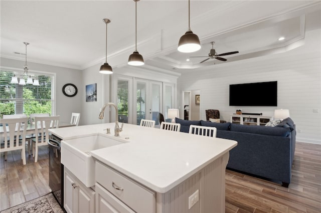 kitchen featuring light wood-type flooring, sink, decorative light fixtures, white cabinets, and an island with sink