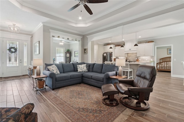 living room with ceiling fan with notable chandelier, light wood-type flooring, and crown molding