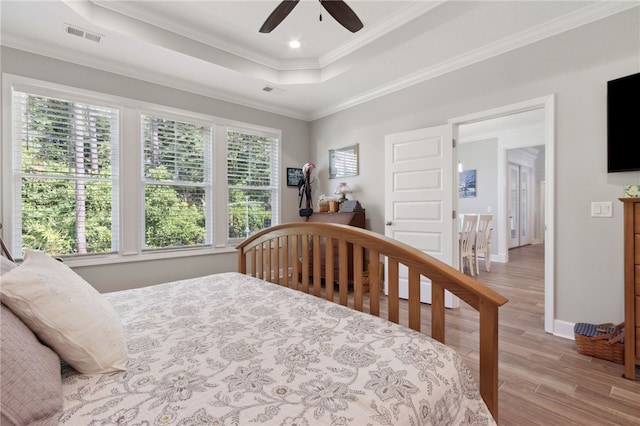 bedroom with ceiling fan, a raised ceiling, ornamental molding, and light hardwood / wood-style flooring