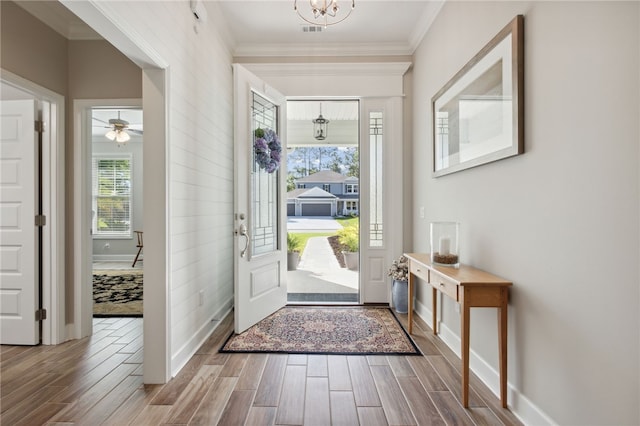 entryway featuring hardwood / wood-style floors, ceiling fan with notable chandelier, and crown molding