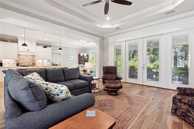 living room featuring ceiling fan with notable chandelier, light hardwood / wood-style floors, a wealth of natural light, and crown molding