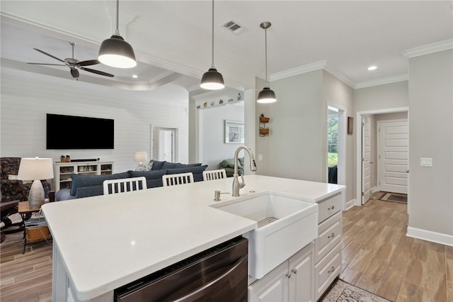 kitchen with light wood-type flooring, stainless steel dishwasher, a kitchen island with sink, pendant lighting, and white cabinets