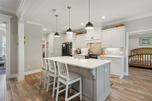 kitchen with decorative light fixtures, stainless steel appliances, white cabinetry, and light hardwood / wood-style flooring