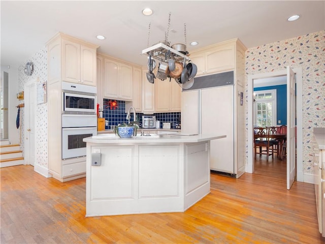 kitchen featuring built in appliances, wallpapered walls, light wood-type flooring, light countertops, and decorative backsplash