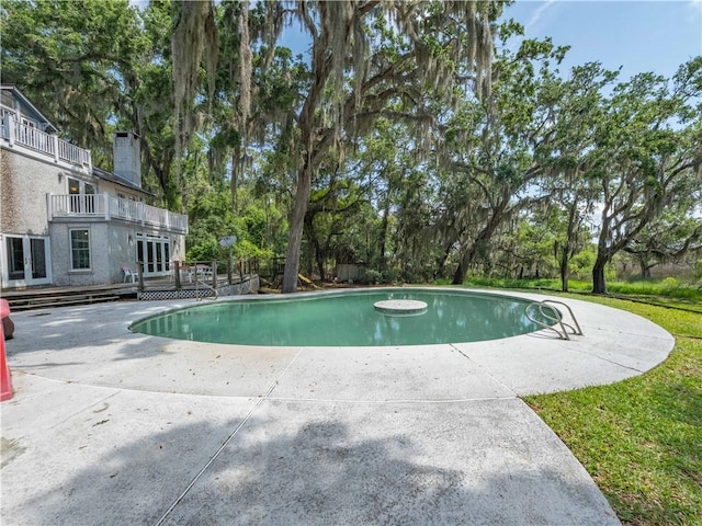 outdoor pool featuring french doors, a patio area, a deck, and view of wooded area