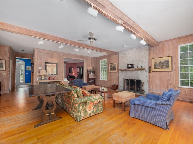 living room with track lighting, wood walls, beam ceiling, wood finished floors, and a fireplace