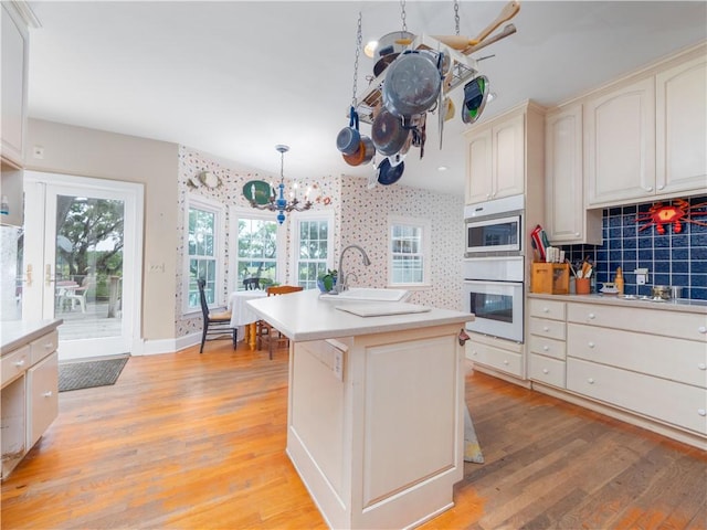 kitchen with white oven, a chandelier, built in microwave, a sink, and light wood-type flooring