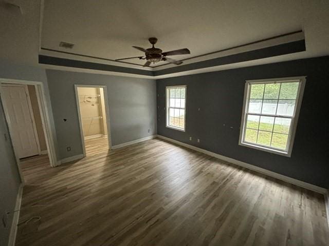 unfurnished bedroom with dark hardwood / wood-style flooring, ceiling fan, and a raised ceiling