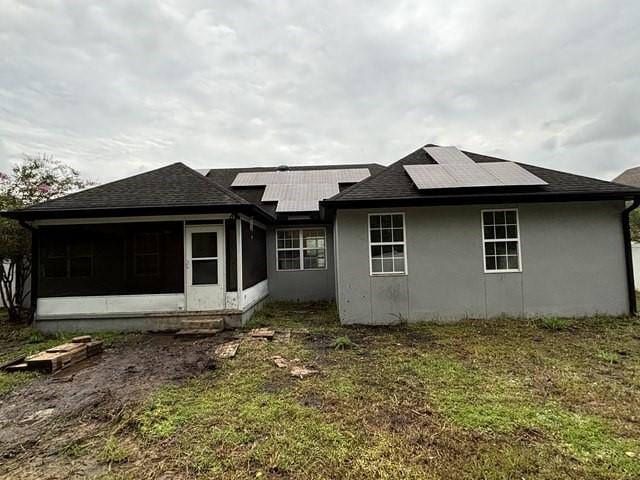 rear view of house featuring a sunroom and solar panels