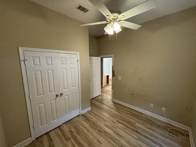 unfurnished bedroom featuring a towering ceiling, a closet, light hardwood / wood-style flooring, and ceiling fan