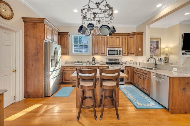 kitchen with appliances with stainless steel finishes, light wood-type flooring, ornamental molding, and sink