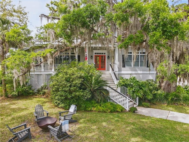 view of property hidden behind natural elements with french doors, a front lawn, and stairway
