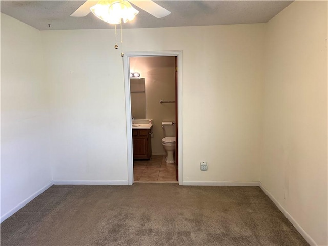 unfurnished bedroom featuring ensuite bath, ceiling fan, and dark carpet