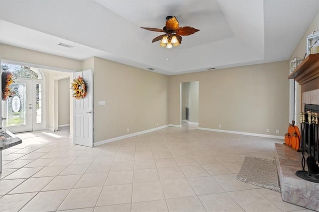 unfurnished living room with a raised ceiling, a fireplace with raised hearth, light tile patterned floors, baseboards, and ceiling fan