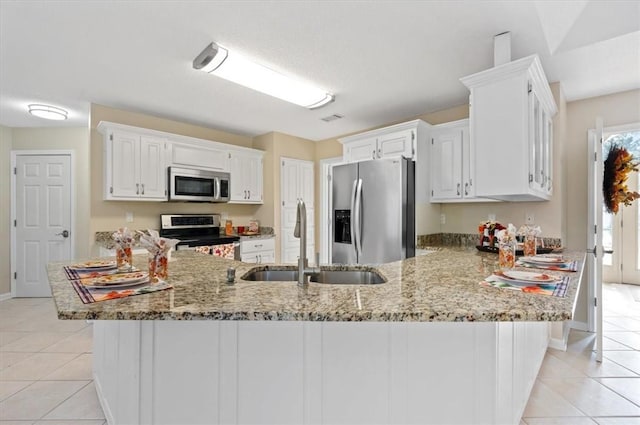 kitchen featuring a sink, light stone counters, appliances with stainless steel finishes, a peninsula, and light tile patterned floors