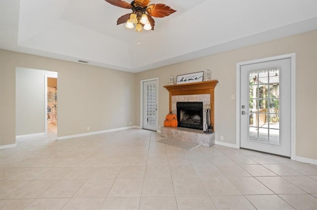 unfurnished living room featuring a raised ceiling, a ceiling fan, light tile patterned floors, baseboards, and a tile fireplace